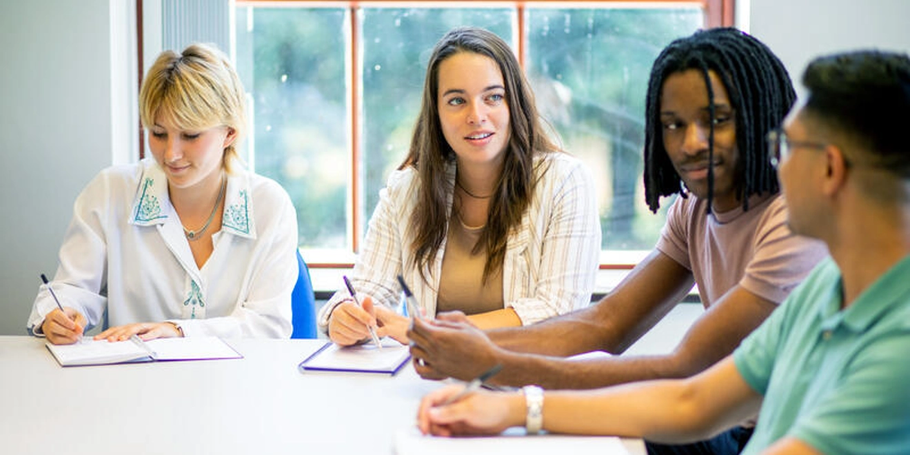 Young people at a table, taking notes and talking to each other